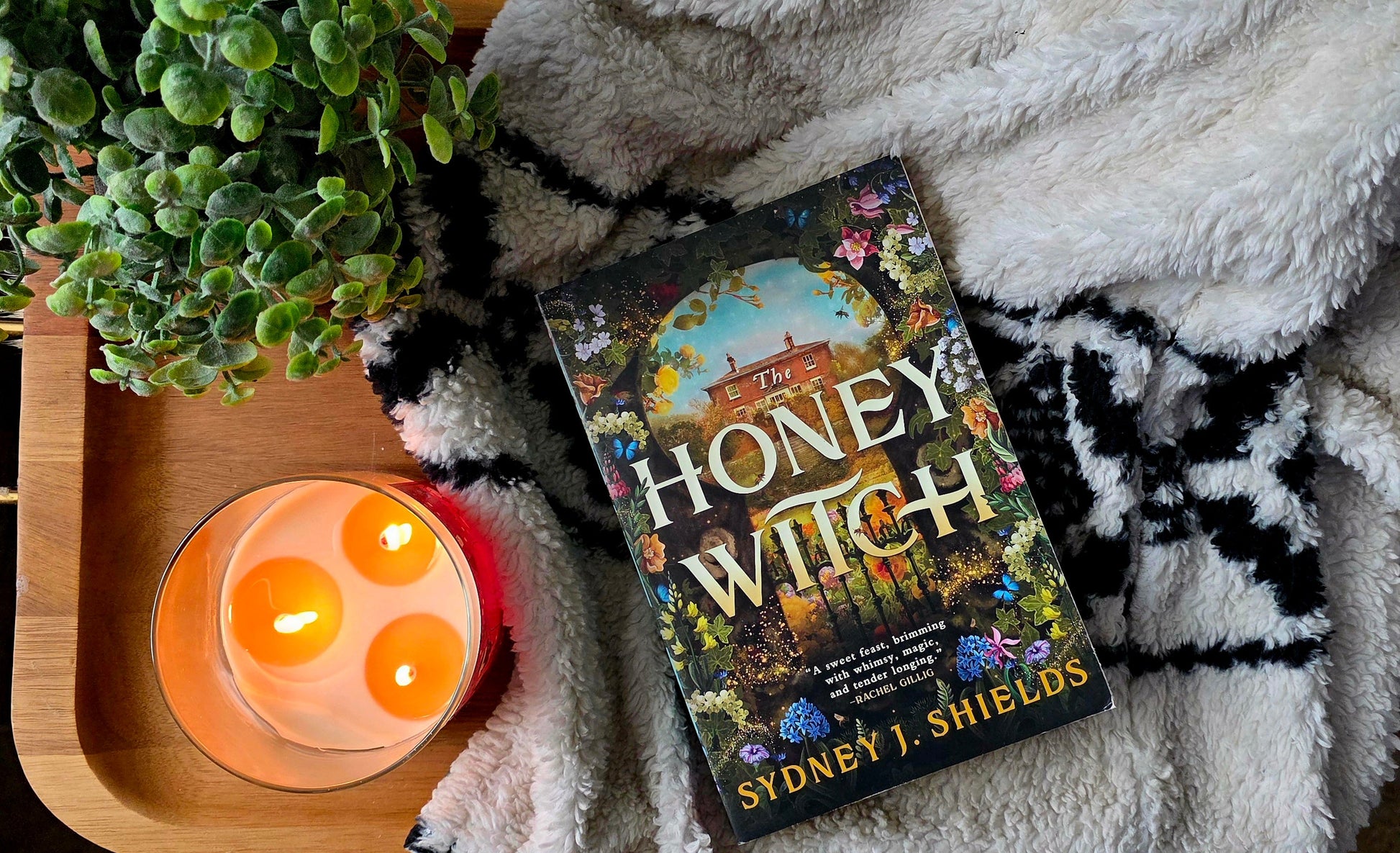 Book titled 'Honey, I'm a Witch' on a blanket with a candle and plant in the background
