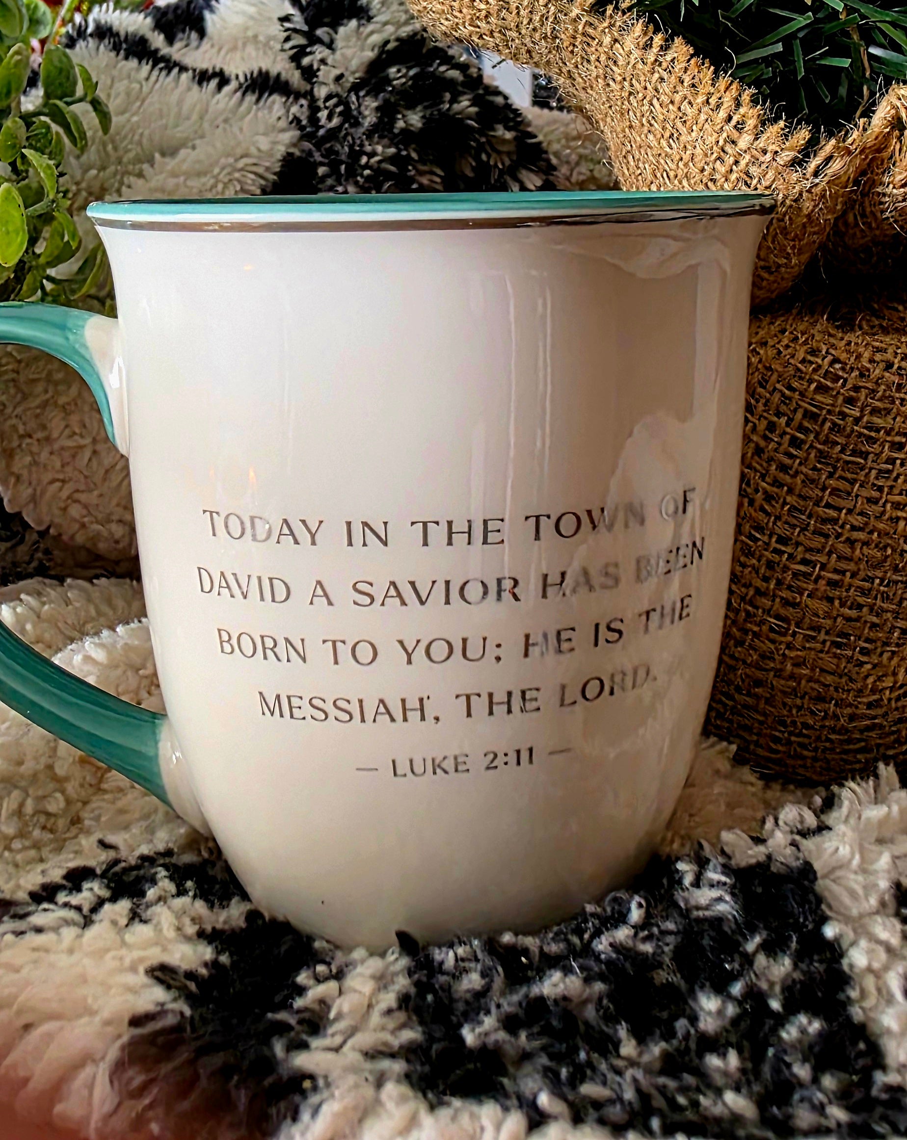 White mug with blue handle featuring a biblical verse on a textured surface with decorative elements.